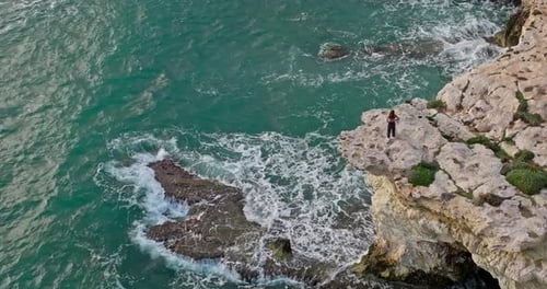 Aerial View of a Young Woman Standing on the Rocks on the Ocean Shore