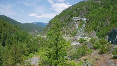 Aerial drone view rising above the trees to reveal a highway and powerlines running through the moun