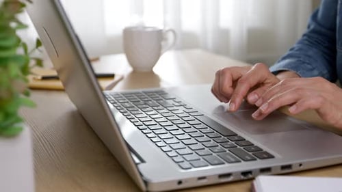 Close-up of a working woman's hands typing on a laptop keyboard.