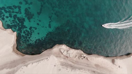 Top shot of patagonian sea close to the shore with cliffs and boat crossing from right to left