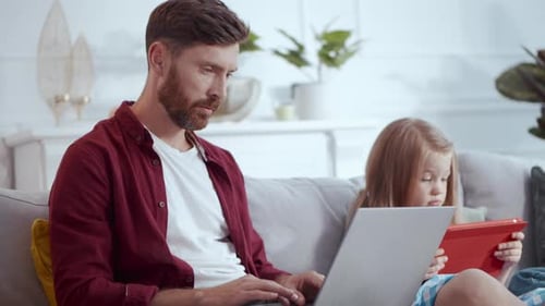 Father and Daughter Using Laptop and Tablet on Couch