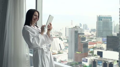 Smiling Woman Using Tablet by City View Window