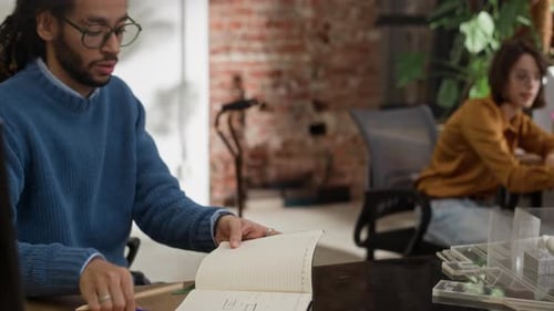 Young Biracial Man Discussing Notes with Colleague in Architectural Office