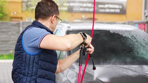 Young Man Washes His Car at a Selfservice Car Wash Using a Hose with Pressurized Water and Foam