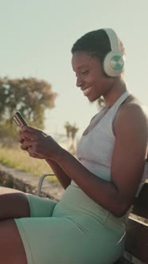 Smiling Woman With Headphones Using Phone on Park Bench