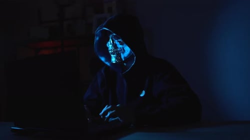 Hacker anônimo com capuz preto trabalhando em um laptop à noite, simbolizando crimes on-line e violação de dados