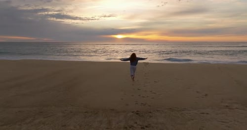 Silhouette of a Woman Running Along the Ocean Coast Barefoot on a Breaking Wave at Sunset The