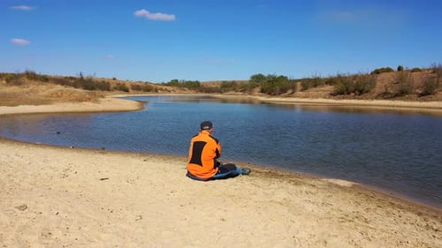 Lone Man Sitting on Sandy Beach by the Water