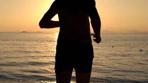 Silhouette of young man running into the sea at sunset in slow motion