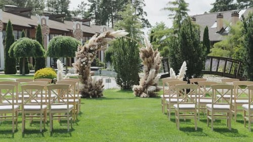 A Wedding in a Lush Field with Wooden Chairs and a Floral Arch