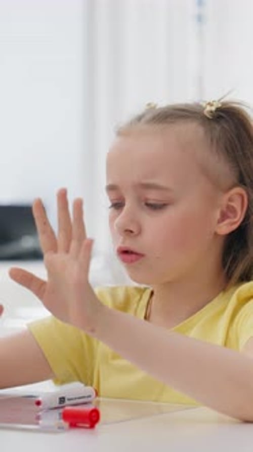 Young Girl Seated at Table Focusing on Her Hands While Speaking