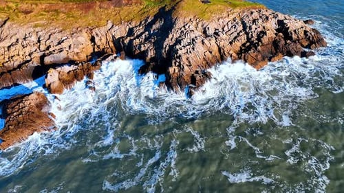 Waves break against a rocky shore in a coastal area during the daytime.