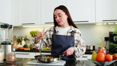 Young Woman Cooking and Tasting Food in Kitchen