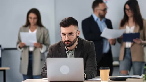 Pensive Man Confidently Working Laptop at Modern Corporate Office with Colleagues Routine Occupation