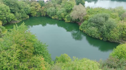 Aerial shot of a serene pond surrounded by lush greenery, reflecting the clear sky, creating a peace