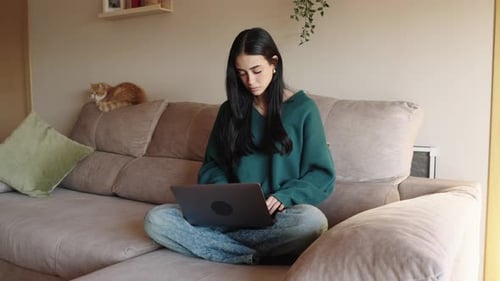 Junge Frau arbeitet aus der Ferne am Laptop mit Katze in der Nähe
