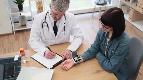 Physician and Woman Monitoring Tonometer on Wrist in Office