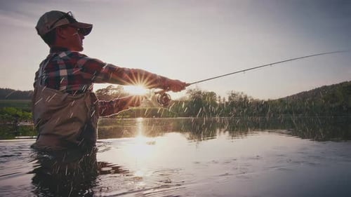 Fly fishing. Angler stands in the river and casts the fly at sunset with splashes