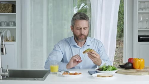 Gray Haired Man Eating Sandwich in Kitchen