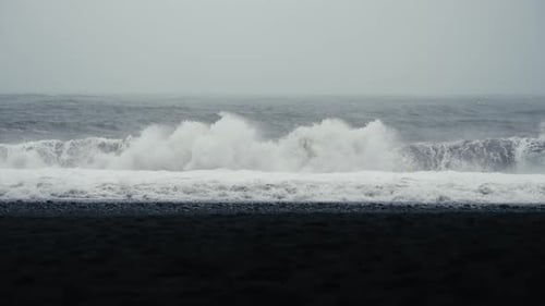 Dark majestic waves crash onto a black sand beach. Reynisfjara Iceland. Shot in glorious slow motion