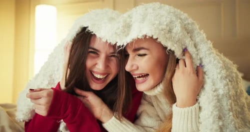 Una alegre chica morena feliz con una chaqueta roja está envuelta en una manta con su novia rubia