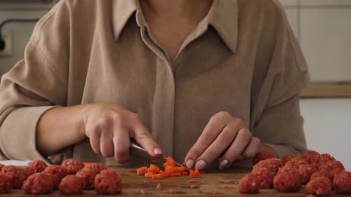 Woman Dices Carrot with Meatballs on Wood Board