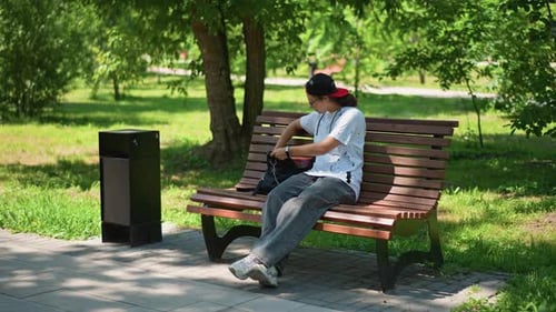 Traveler Uses Smartphone Man Relaxes on Park Bench While Viewing His Phone Young Traveler Seated on