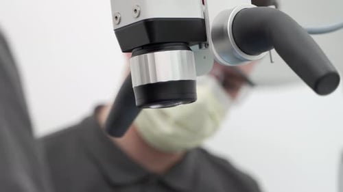 Primer plano de un dentista masculino con un paciente asistente utilizando un microscopio dental durante la operación en el