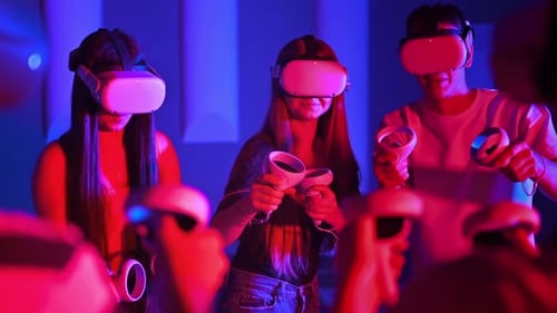 A team of young friends play virtual reality games in VR equipment on an arena. Neon lights