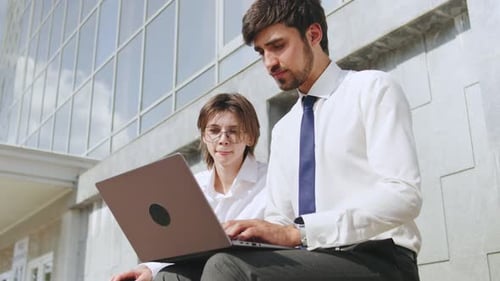 Geschäftsleute arbeiten im Freien auf einem Laptop zusammen und tauschen Ideen in einer hellen urbanen Umgebung aus
