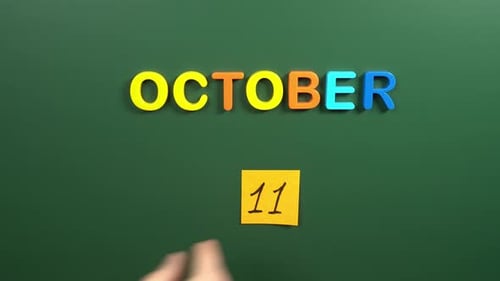 Hand sticking a sticker 11 October calendar day on school board. 11 date of October. Eleventh day