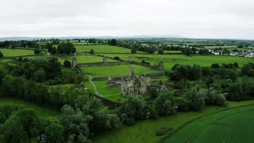 Drone shot pulling away from Ireland's Kells Priory surrounded by green foliage.