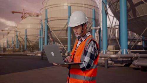 Side View Of Asian Male Engineer Working On A Laptop with Spherical Tank