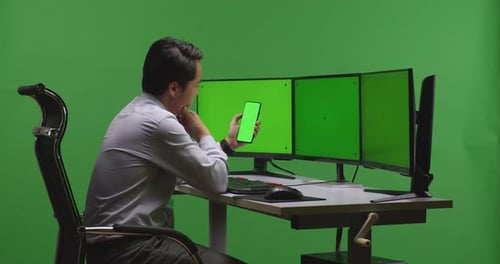 Asian Man Working On Mobile Phone And Multiple Monitor With Mock Up Green Screen In Green Screen