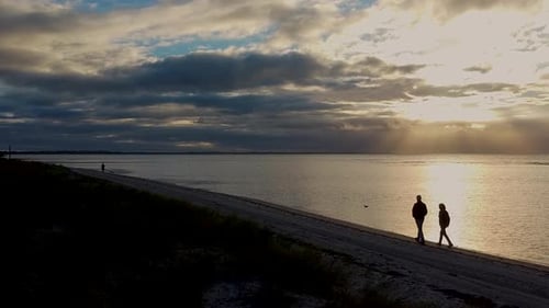Romantic shot a couple walking along the beach at sunset on a calm day with no waves