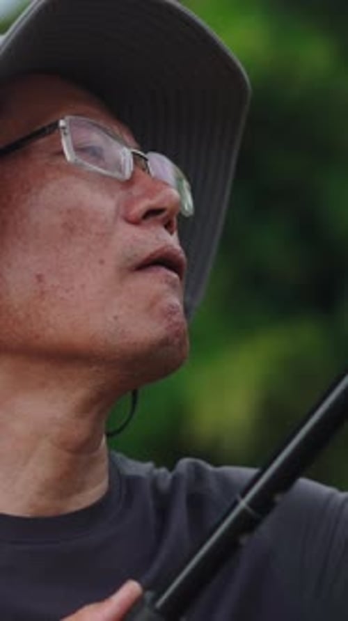 Closeup do rosto de um fotógrafo asiático maduro com óculos e chapéu ajustando sua câmera