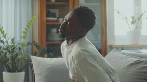 Sick Black Man Clutching Upset Stomach in Pain on Couch at Home