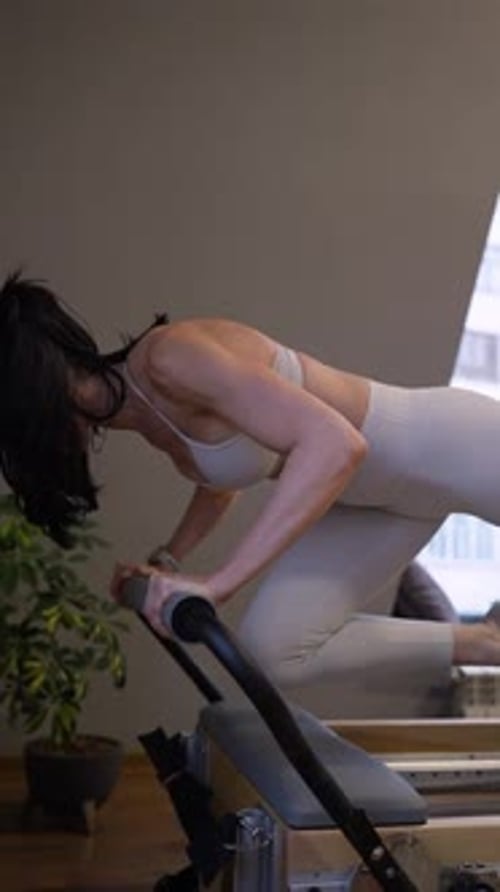Woman in Light Gym Clothes Doing Pilates Pushups Stretches on Reformer Knee Bent in Indoor Studio