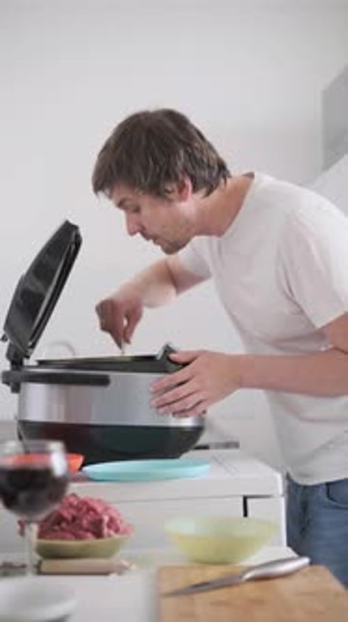 Homme remuant les aliments dans un multicuiseur avec spatule, cuisine maison dans une cuisine moderne lumineuse, vie décontractée