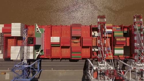 Frachtschiff beladen mit bunten Containern, das an einem belebten Hafen angedockt ist, Luftaufnahme