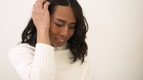 Confident young transgender woman smiling in studio portrait with hand in hair