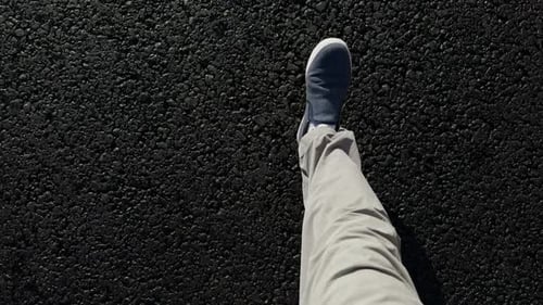 Zeitlupenaufnahmen von oben: Füße von Männern in Turnschuhen und grauen Hosen, die auf frischem Asphalt laufen
