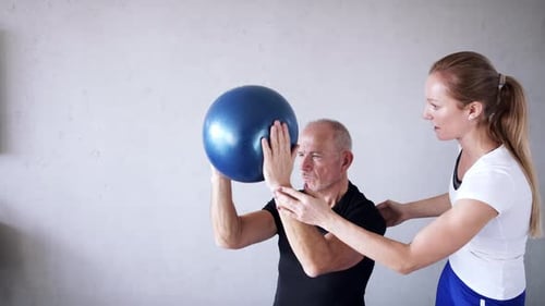 Senior Man Exercises with Trainer and Exercise Ball