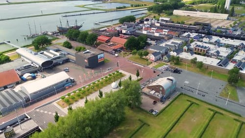 An aerial view of a coastal town with a harbor, colorful buildings and a replica ship docked along