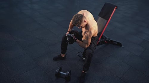 Bodybuilder training in gym. Young sportsman pumping arm muscles with a dumbbell.