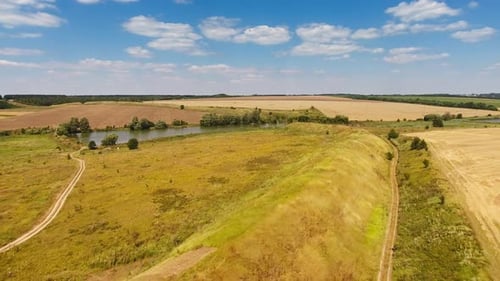 Long hill separating meadows from farmlands. Little pond in the middle of the fields.