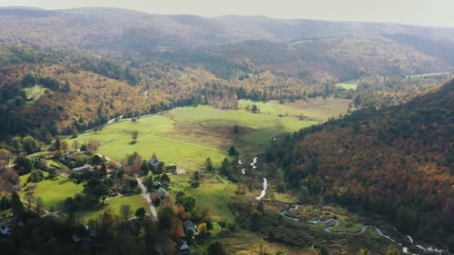 Aerial forwarding shot of rural landscape with the view of a village by the side of hills covered wi