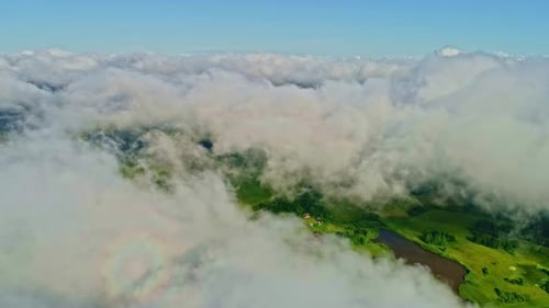 Drone flying over clouds capturing green pasture land during daytime. Cloudscape.