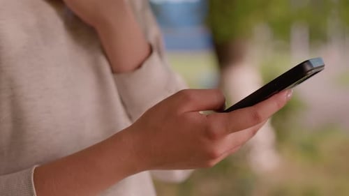 CloseUp of Hand Using Smartphone Outdoors with Blurred Green Background