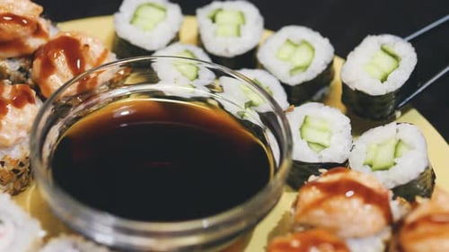Taking a Sushi Roll with Black Chopsticks and Dipping It in Soy Sauce